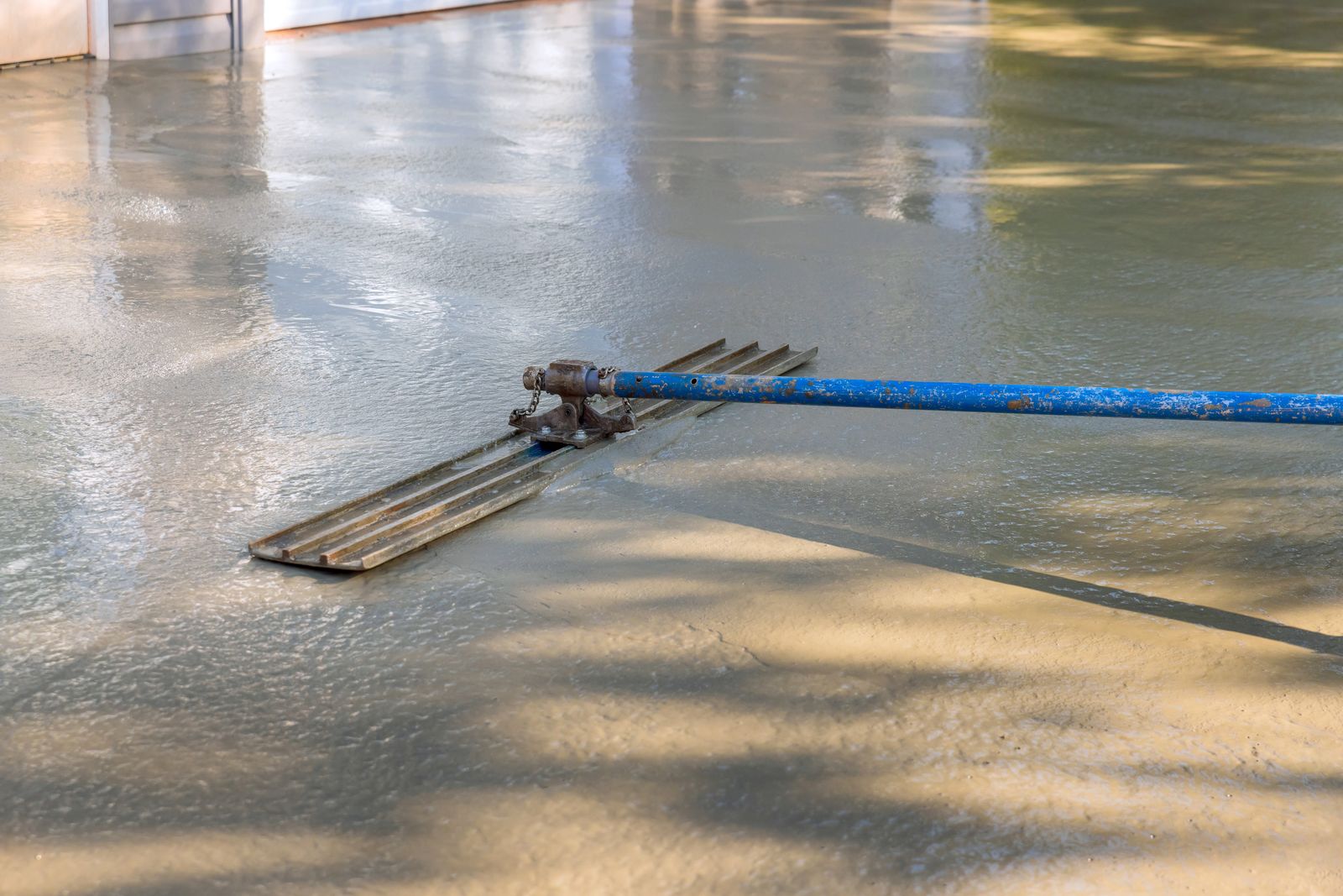 A contractor screeding a freshly poured concrete slab smooth with a long bull float.